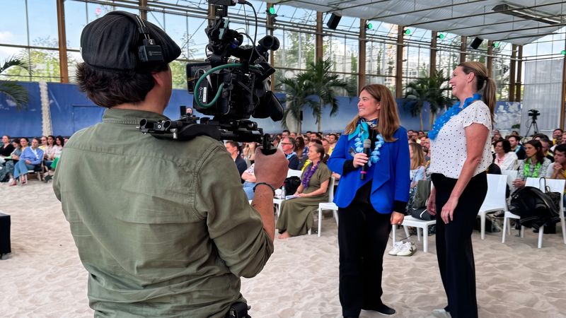 Kameraoperator mit Schulterkamera filmt zwei Personen auf einer Veranstaltung mit Publikum