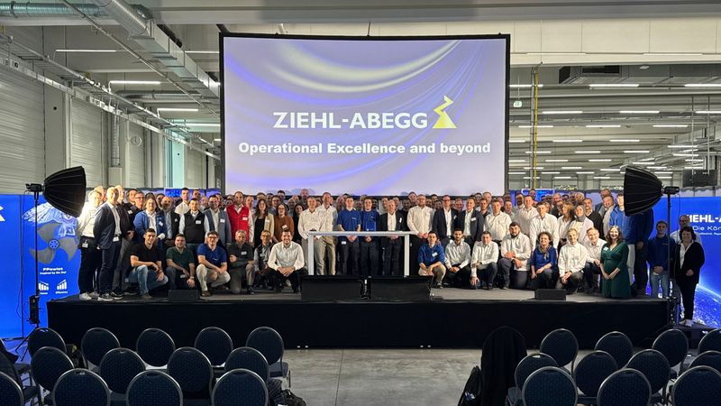 Gruppenfoto der Belegschaft vor einer Bühne in einer Produktionshalle